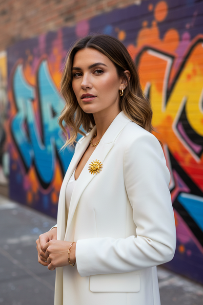 Broche soleil visage dorée portée sur un blazer blanc, fond street art coloré – bijou fantaisie femme Chéri Chérie